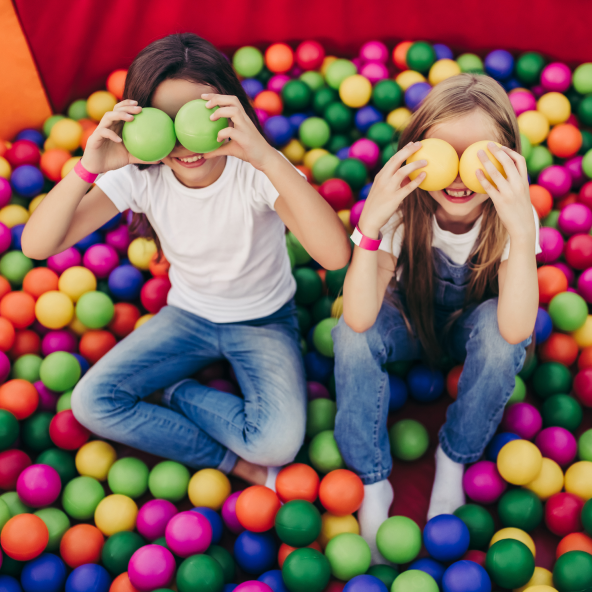 Chłopiec i dziewczynka siedzą w basenie w piłkami kolorowymi i trzymają w obu rękach piłeczki, którymi zasłaniają oczy.